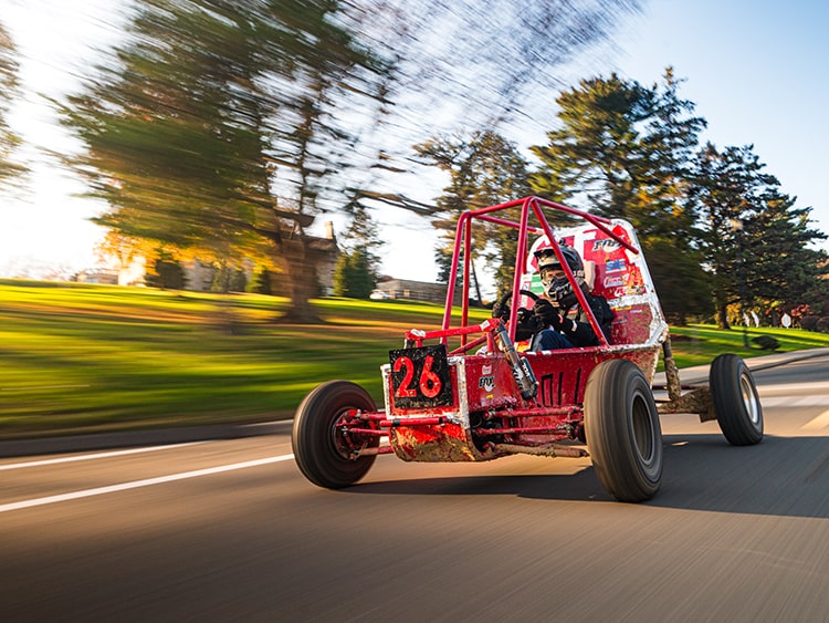 Action shot of a speedy, red Baja buggy as it races down a road past the camera.