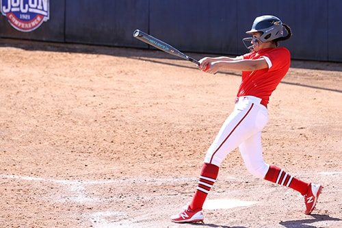 A softball player in a red jersey follows through with a swing of her bat.