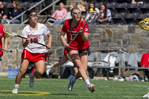 A lacrosse player in a red jersey that reads “Fairfield 17” runs with a ball in her lacrosse stick.