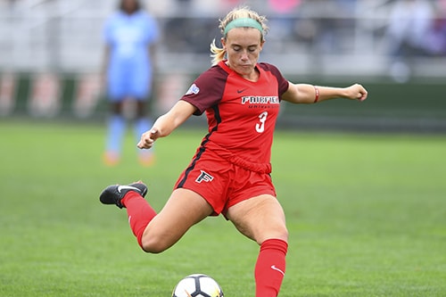 A soccer player in a red jersey that reads “Fairfield 3” prepares to kick a soccer ball. 