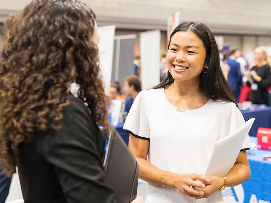 A student in a white dress shirt speaks with an employer at a career fair