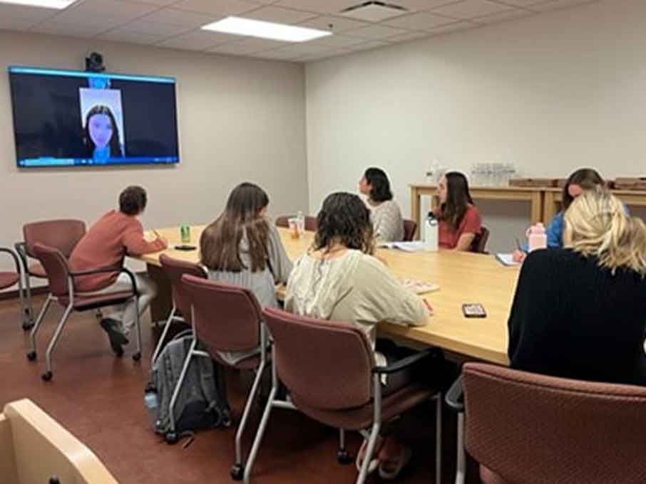 A diverse group of professionals engaged in discussion around a conference table in a modern meeting room.