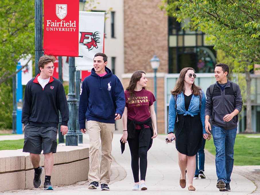 A group of students walking together on a sidewalk at Fairfield University, engaged in conversation and enjoying their time outdoors.