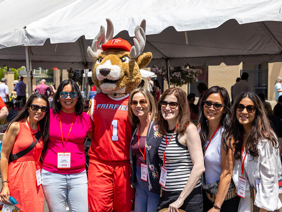 A group of alumni wearing lanyards pose for a photo with Lucas the Stag.