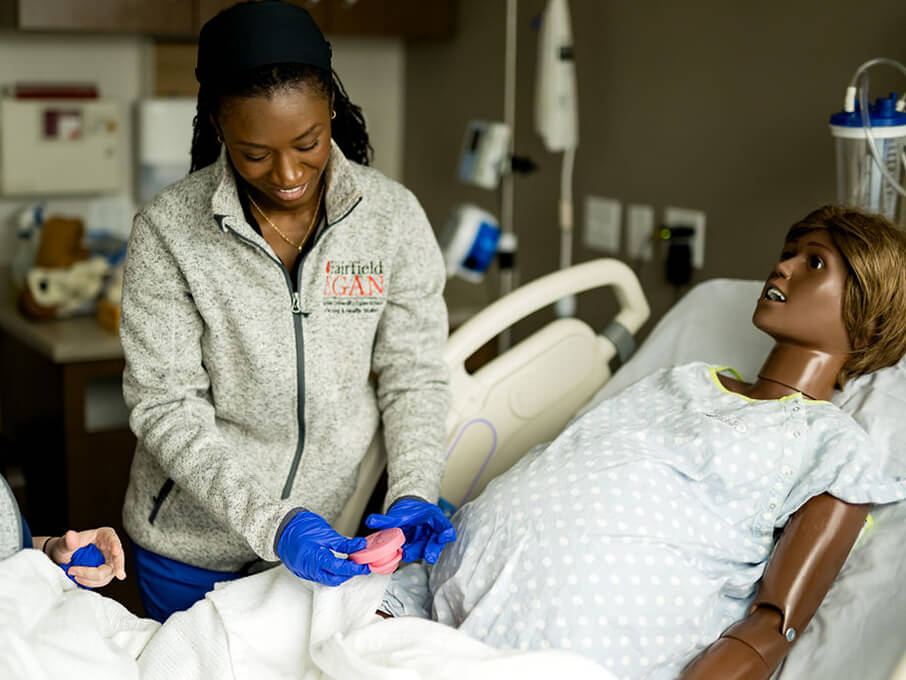 Two students perform a medical exam on a mannequin. 