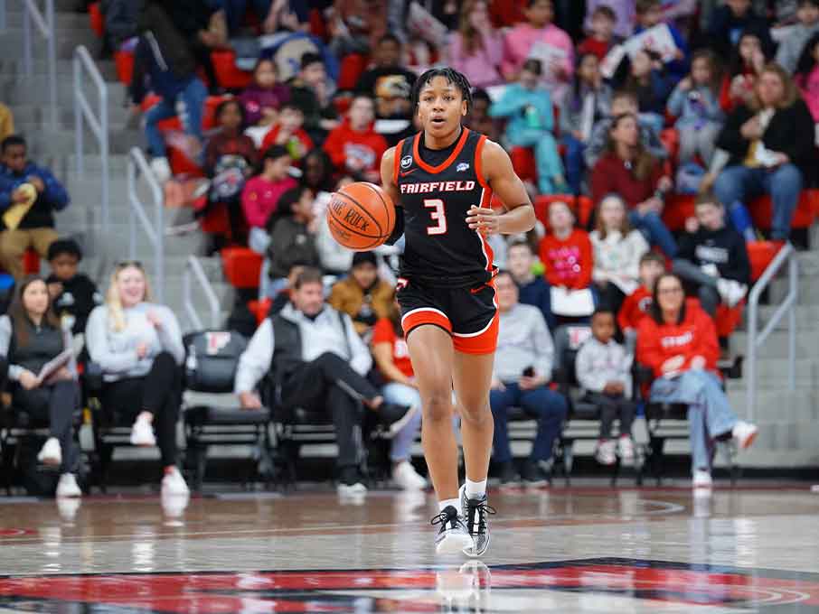 A woman in a black and red uniform dribbles a basketball on the court, showcasing her athletic skills.