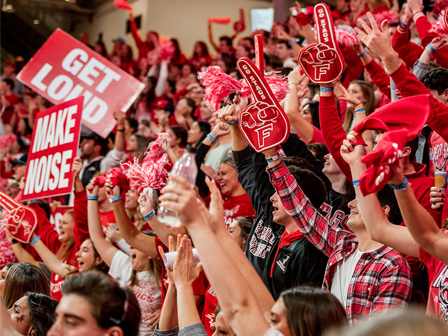 A large crowd in a stadium holds red and white signs, creating a vibrant and energetic atmosphere.