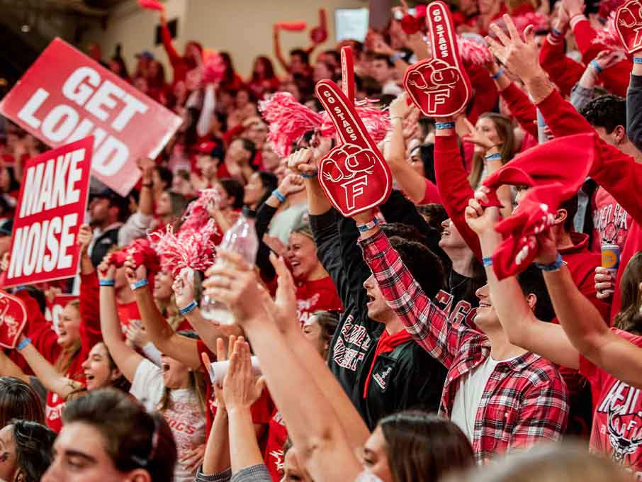 A lively crowd in red shirts waves pom poms, enthusiastically cheering at an event.