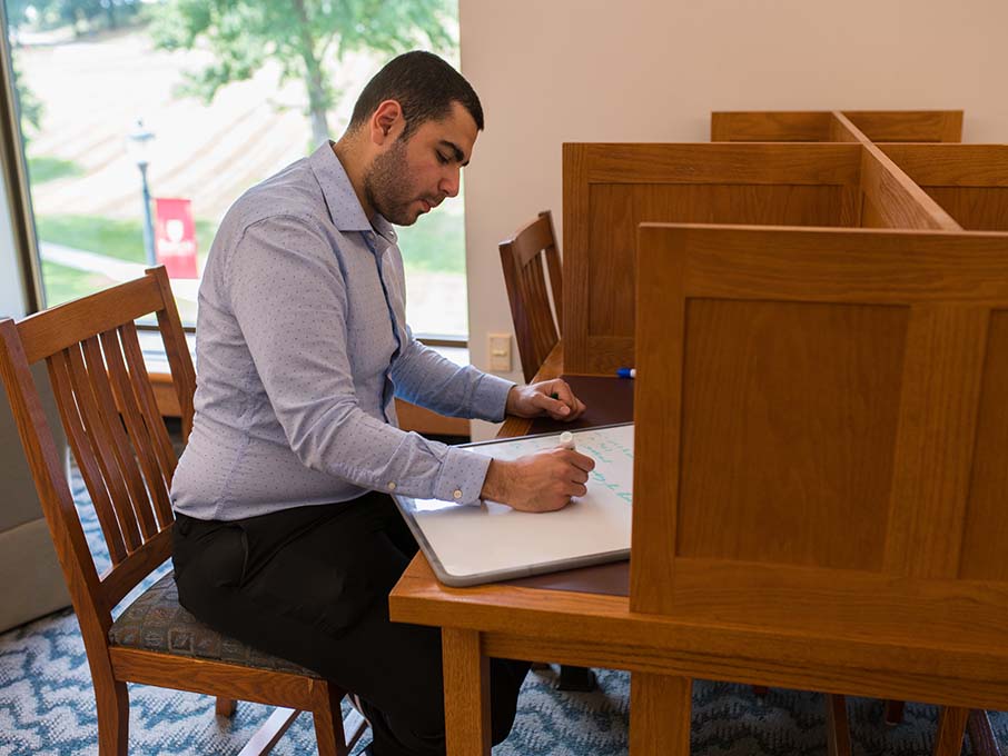 A student sits with Professor Gayle Alberda on a wooden bench and look at a laptop.