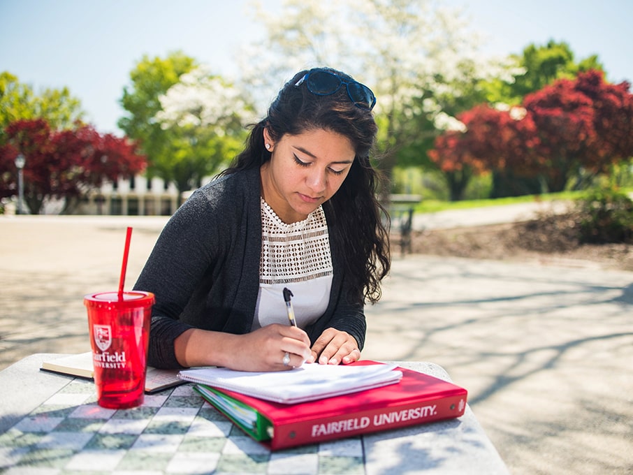 Student doing written homework outside at a table.