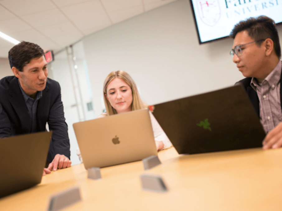 Image of two male students look a female classmates laptop in a classroom