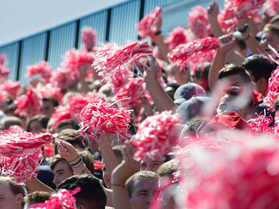 Student cheering with red pompoms at a lacrosse game.