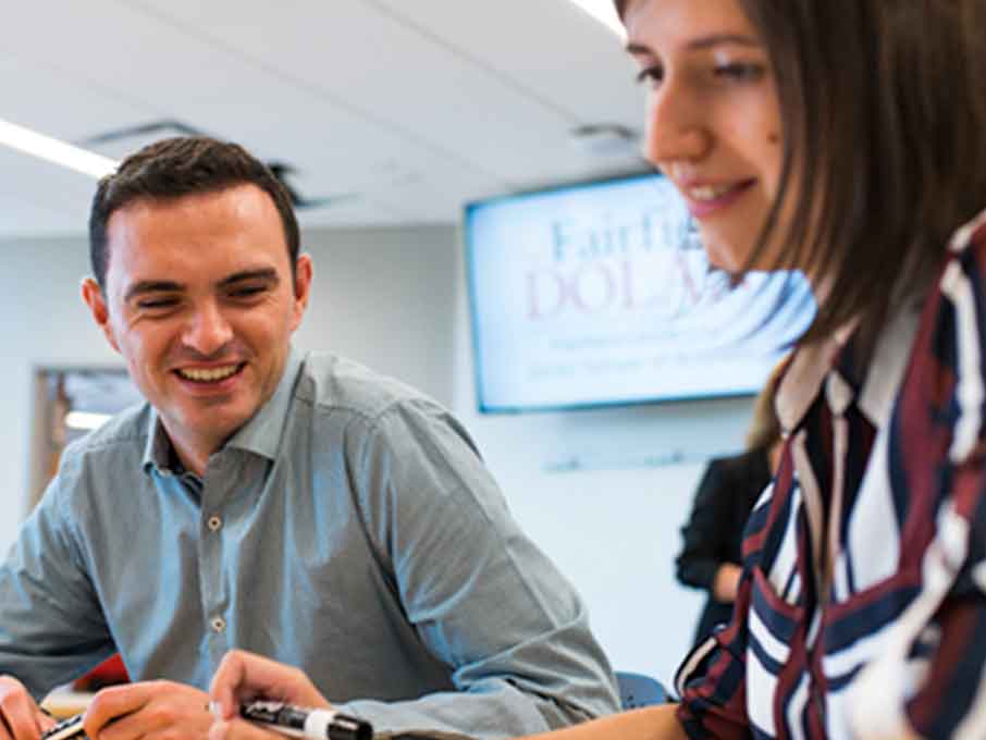 Two students laugh in a classroom with a screen behind them that reads “Fairfield Dolan”.