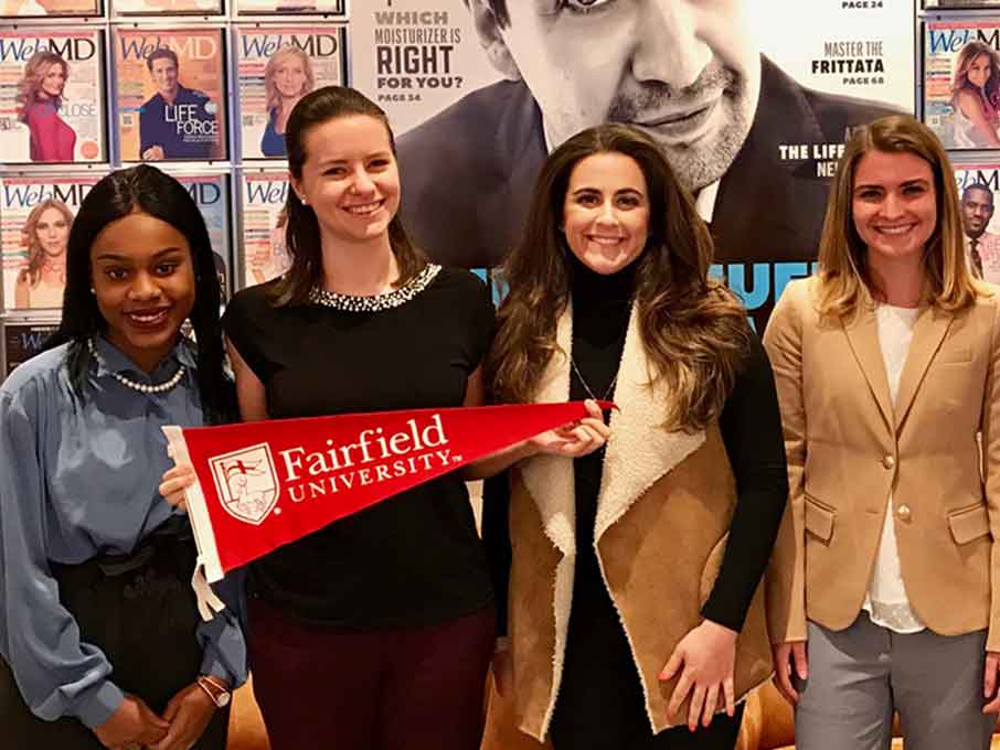 A group of people stand together holding a Fairfield flag in front of a wall of WebMD magazines.