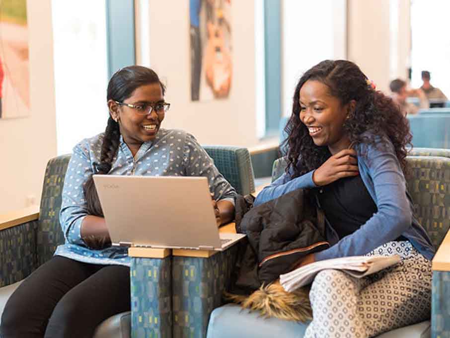 two Fairfield University students sit in campus center looking at a laptop and smiling