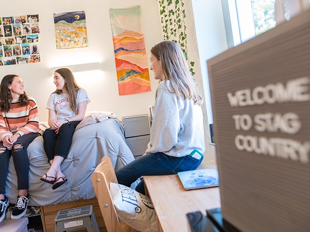 Three students sitting and talking in a residence hall room.