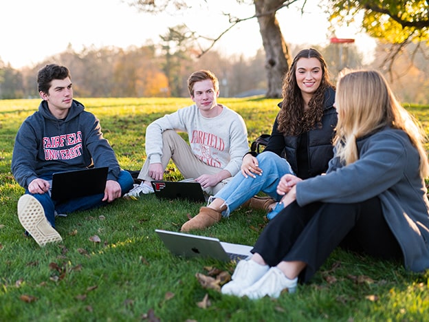 Four students sitting on a hill with laptops.