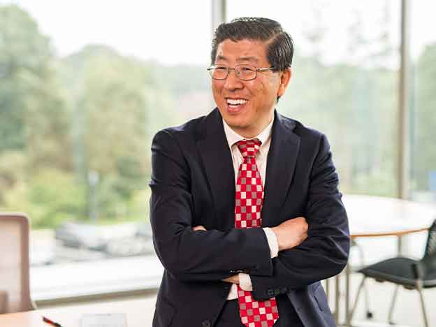 Zhan Li leaning on desk smiling.