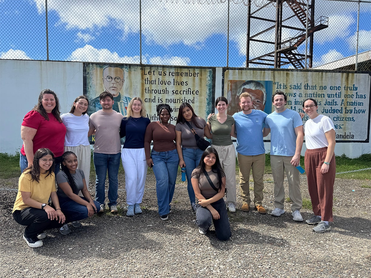 Fairfield students taking a group photo in front of a border fence with inspirational quotes painted on the walls.