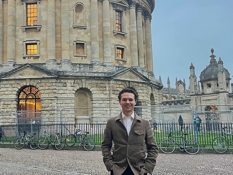 Fairfield student standing on cobblestone outside the circular column structure/area of Blackfriars Hall.