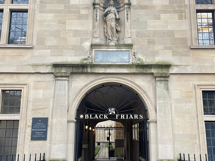 Brick exterior with black, iron gates and a tunnel entryway of Blackfriars Hall, Oxford University.