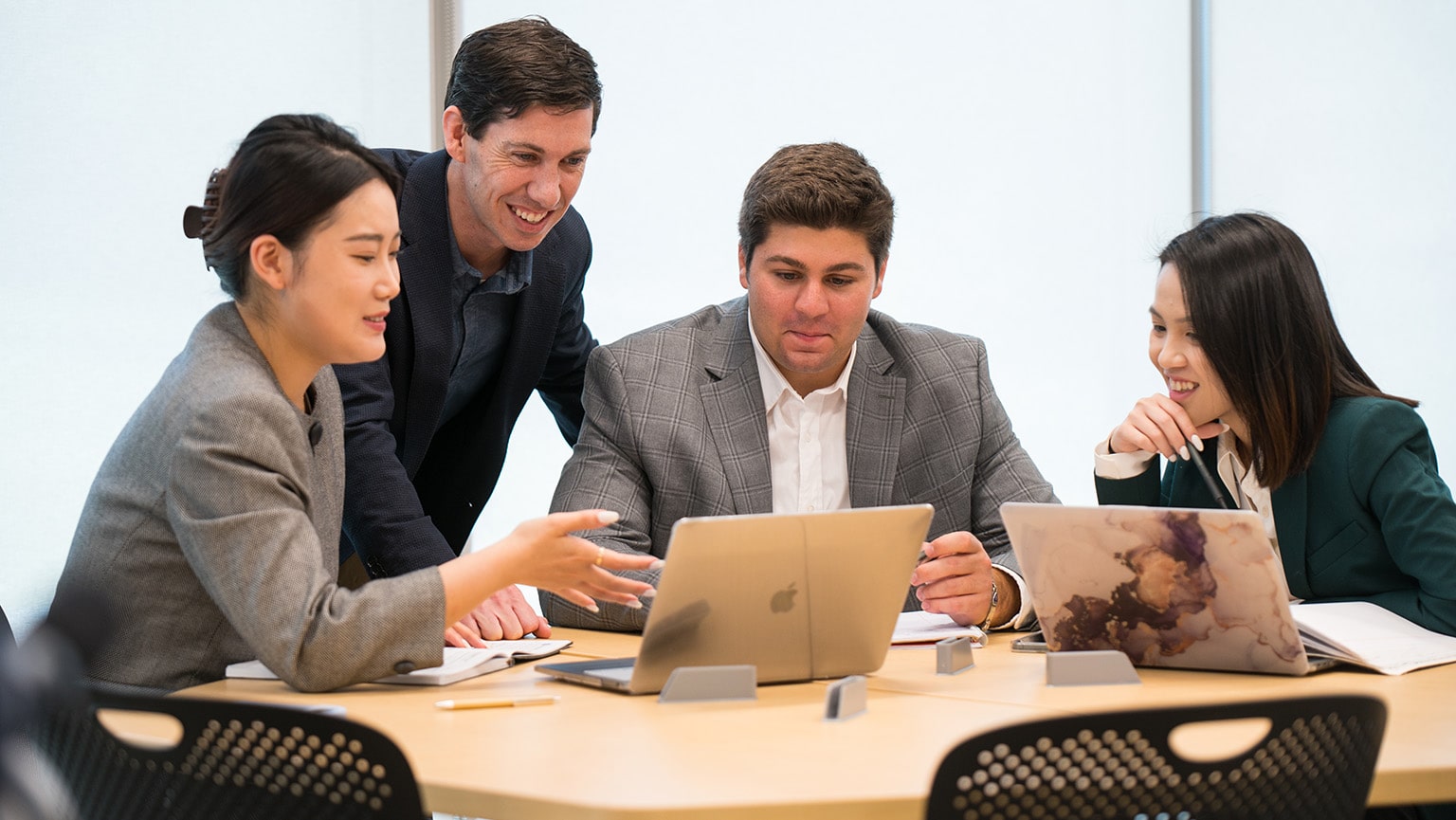 Professional, graduate students working on a group project while seated with their laptops at a round oak table.