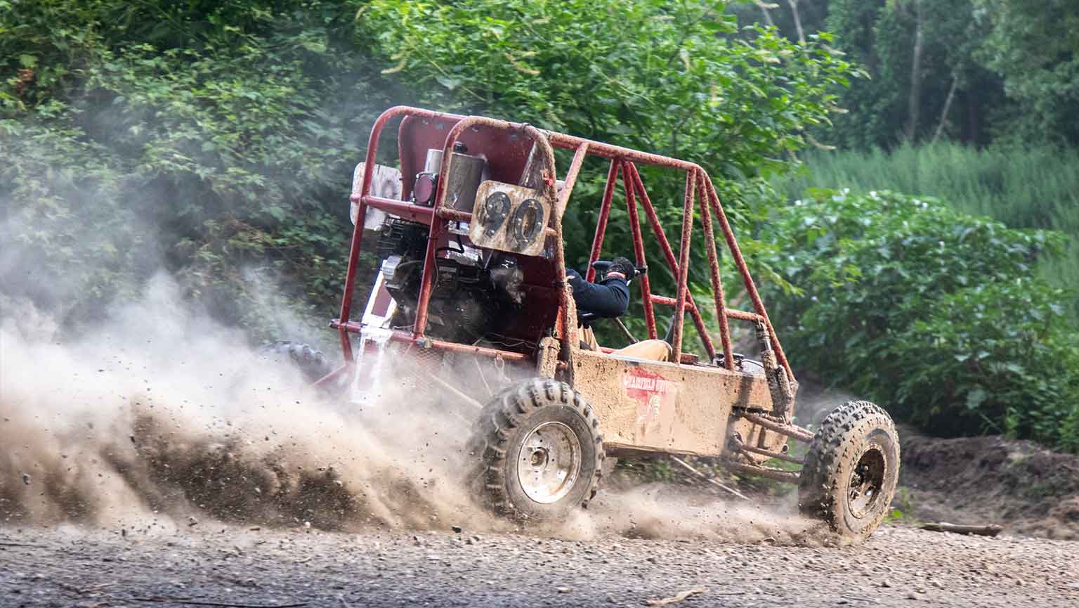 Baja buggy driving on dirt road with a trail of dust.