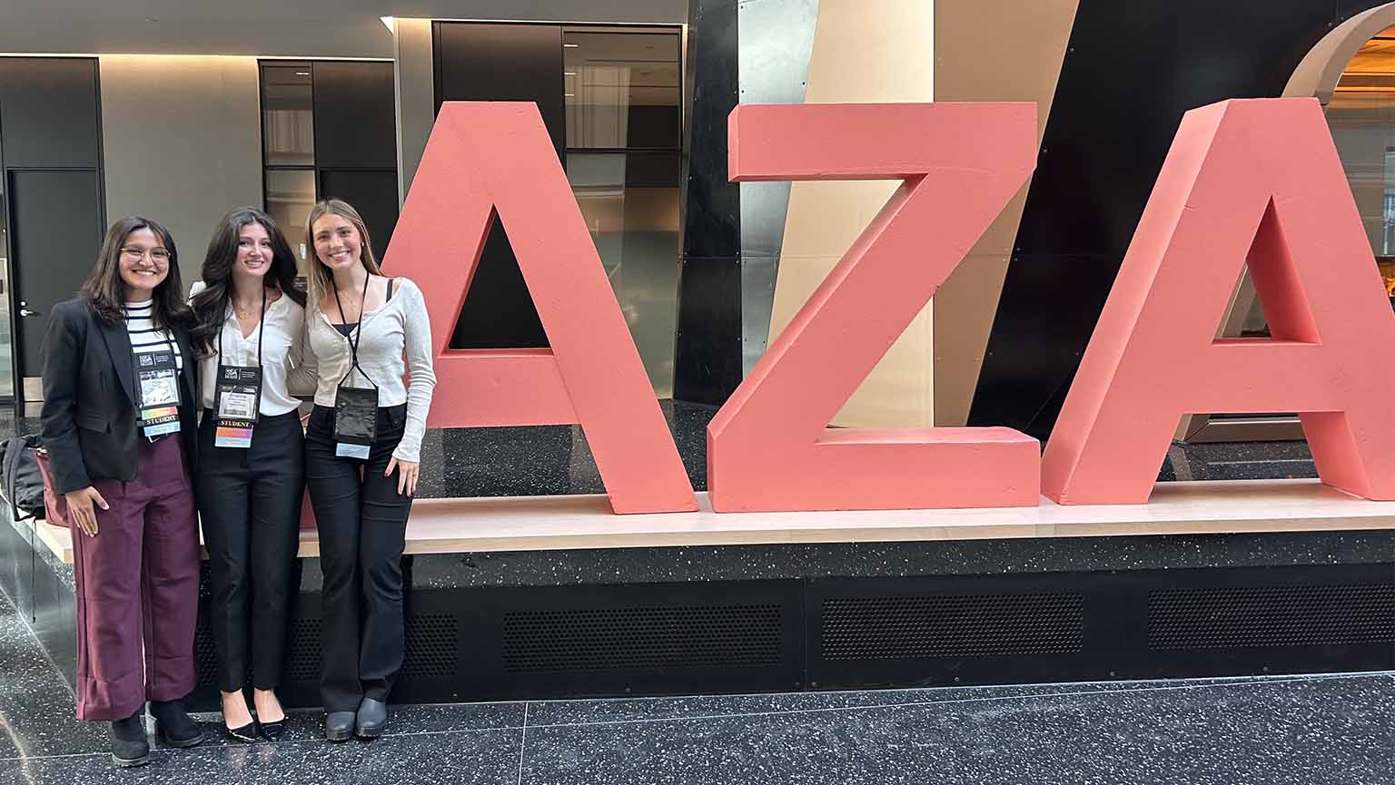 Three students standing next to a large AZA sign at a conference.