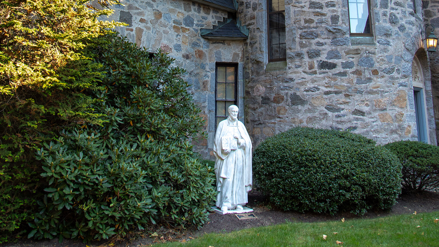 A statue of a man stands prominently in front of a historic stone building, showcasing intricate architectural details.