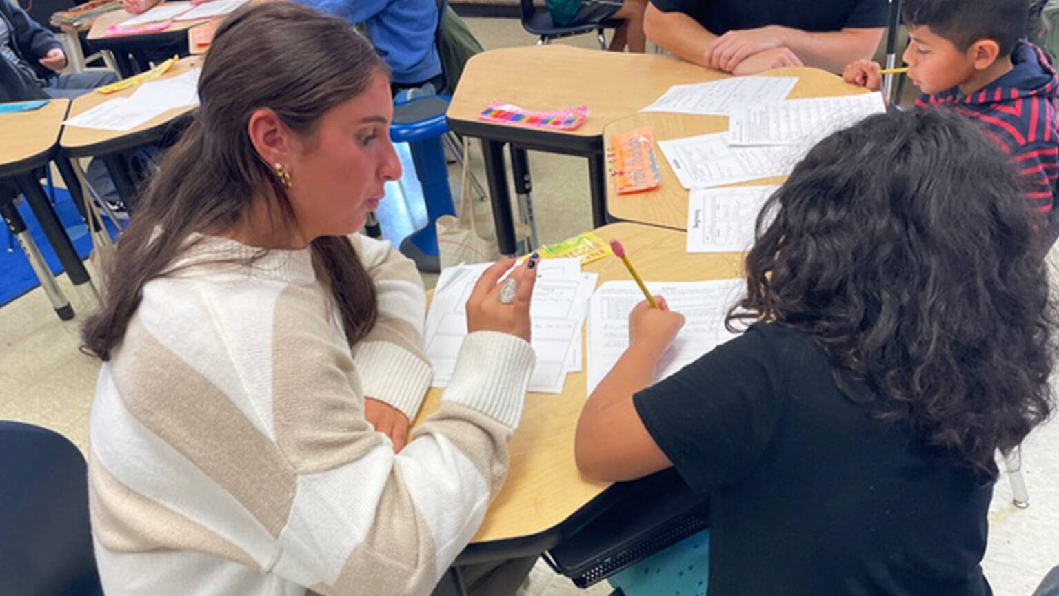 In a classroom, a student teacher provides guidance to a student as they work on homework together.