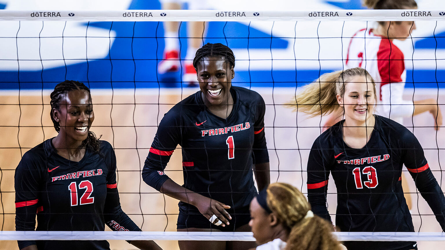 Action shot of three volleyball student-athletes smiling through the net after scoring a point.