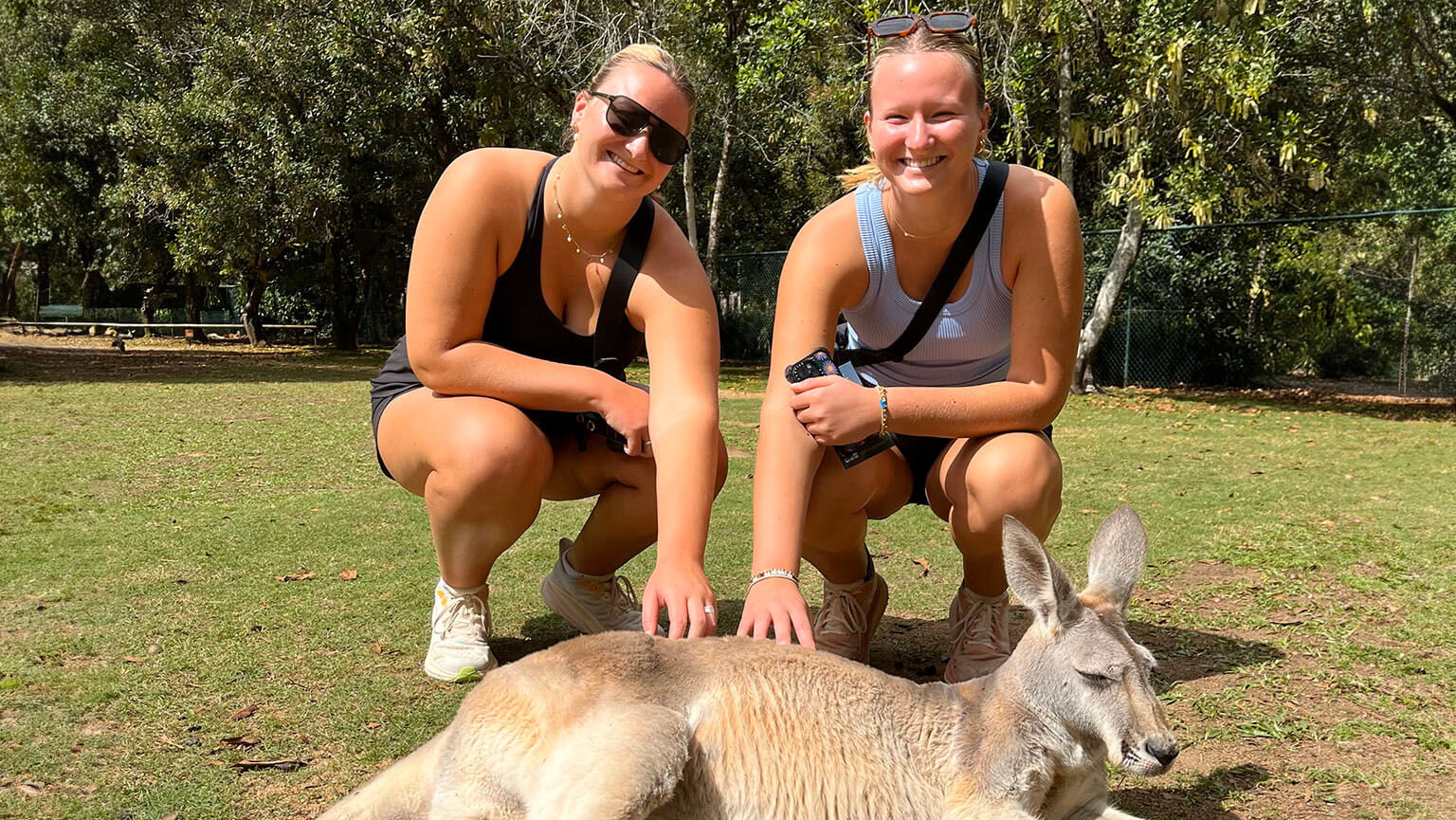 Twins Amelia and Grace Stencel kneel and pose with a lounging zoo kangaroo.