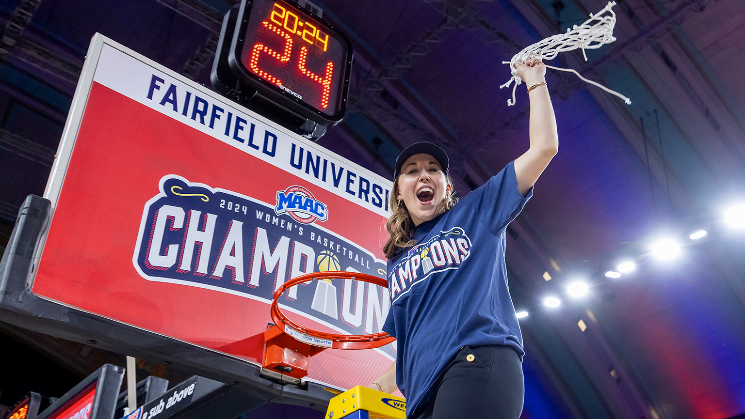 Coach Carly Thibault-DuDonis standing on ladder cutting down basketball net.