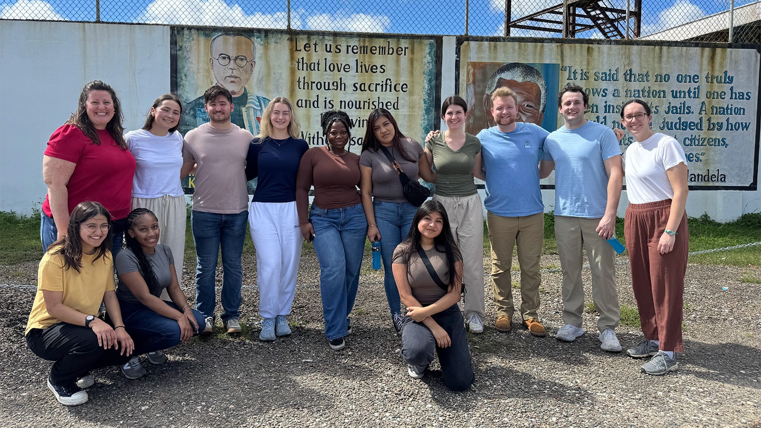 Fairfield students taking a group photo in front of a border fence with inspirational quotes painted on the walls.