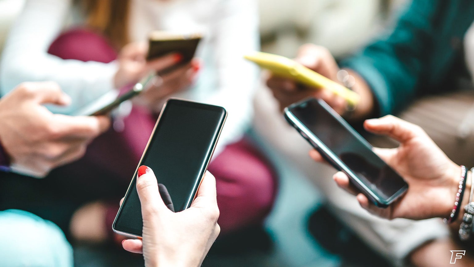 Group of teens sitting in a circle while scrolling on their mobile phones.