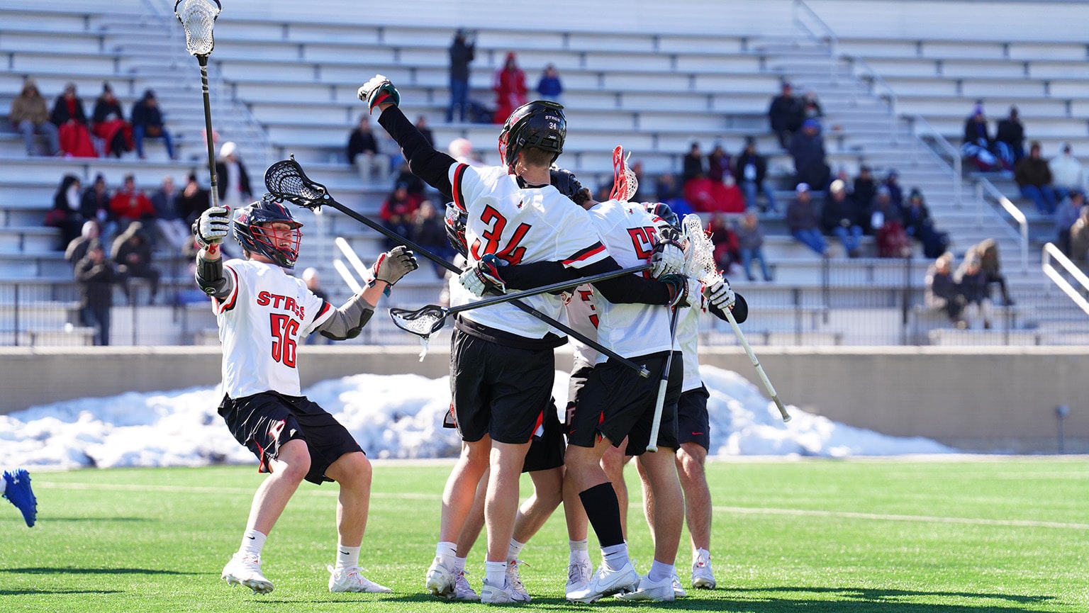 Men's lacrosse student-athletes hugging on the field and celebrating a win.