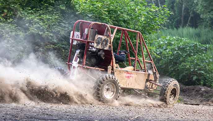 Baja buggy driving on dirt road with a trail of dust.