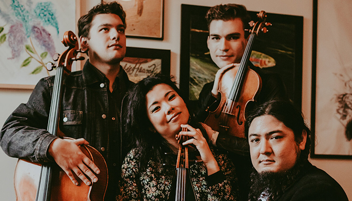 Four individuals of the chamber quartet Owls smiling for a photo showcasing their musical instruments together.  