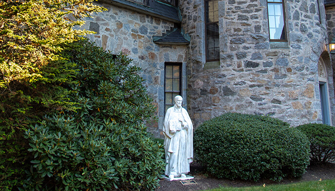 A statue of a man stands prominently in front of a historic stone building, showcasing intricate architectural details.