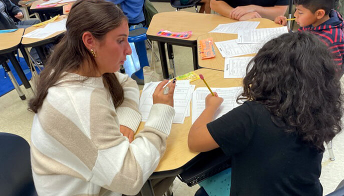 In a classroom, a student teacher provides guidance to a student as they work on homework together.