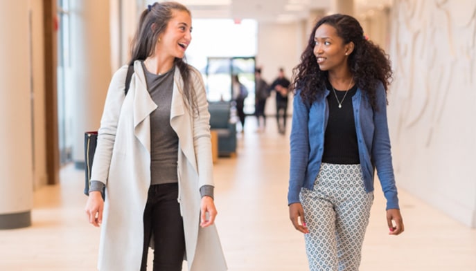 Two students walking next to each other talking.