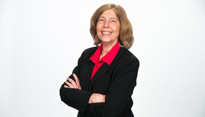 Janet Canepa '82 standing up with arms crossed looking at camera. 