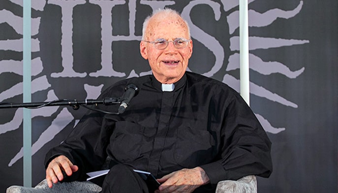 Rev. Charles H. Allen, S.J. sitting down in chair in front of a mic.