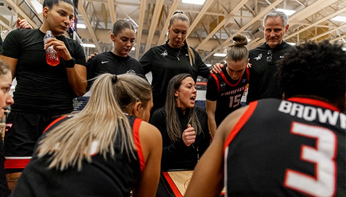 Women's Basketball Coach Carly Thibault-DuDonis giving a pep-talk to her team during a game break.