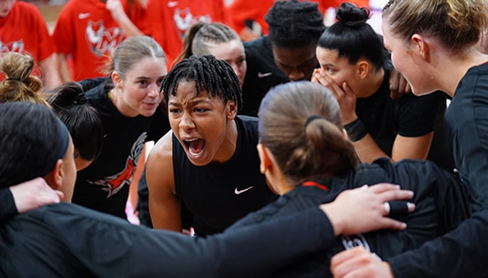 Janelle Brown '24 and teammates in an on-court huddle.