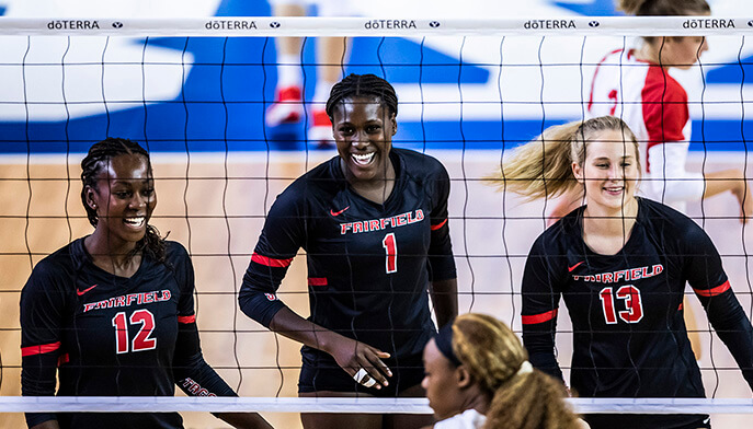 Action shot of three volleyball student-athletes smiling through the net after scoring a point.