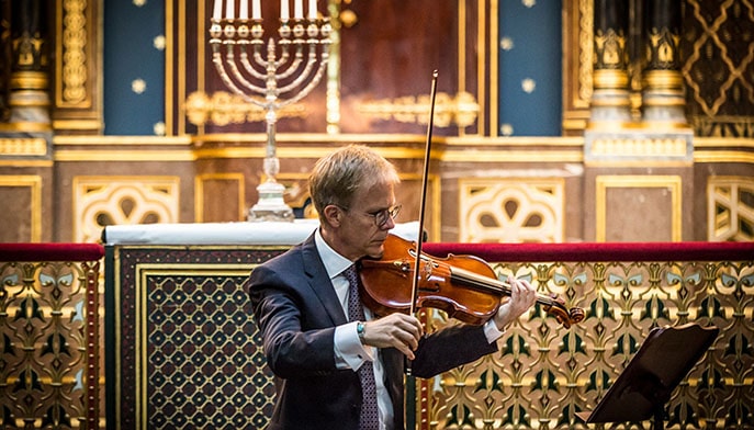 Older man playing the violin in the center of a highly-decorated church.