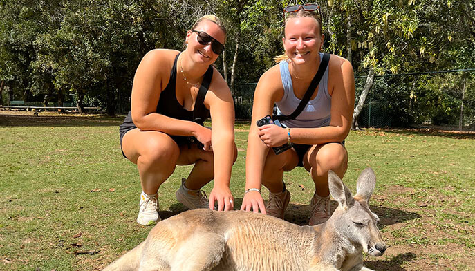 Twins Amelia and Grace Stencel kneel and pose with a lounging zoo kangaroo.