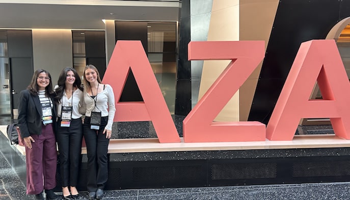 Three students standing next to a large AZA sign at a conference.