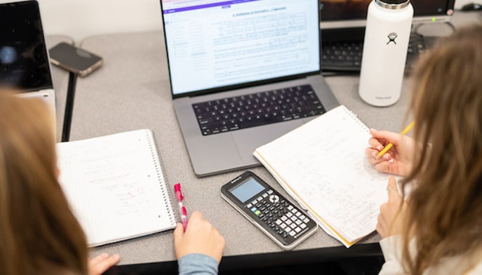 shot of two students working off a laptop and sharing notes in library 